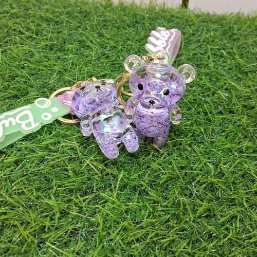 Purple teddy bear keychains on a grassy surface with a 'mga' tag.