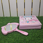 Pink 'My Melody' hand mirror and box on grass with white fence background