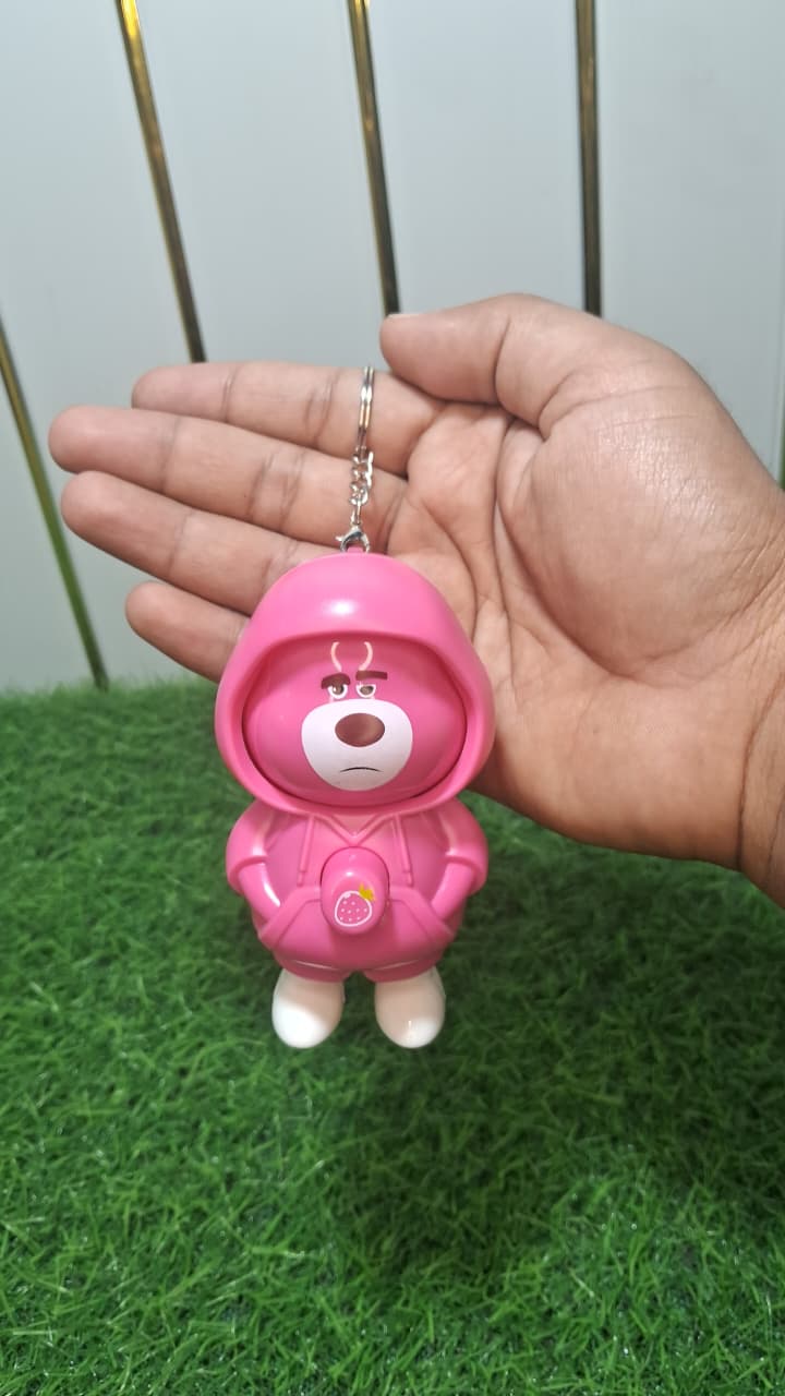 Pink cartoon character keychain held in a hand against a green grassy background