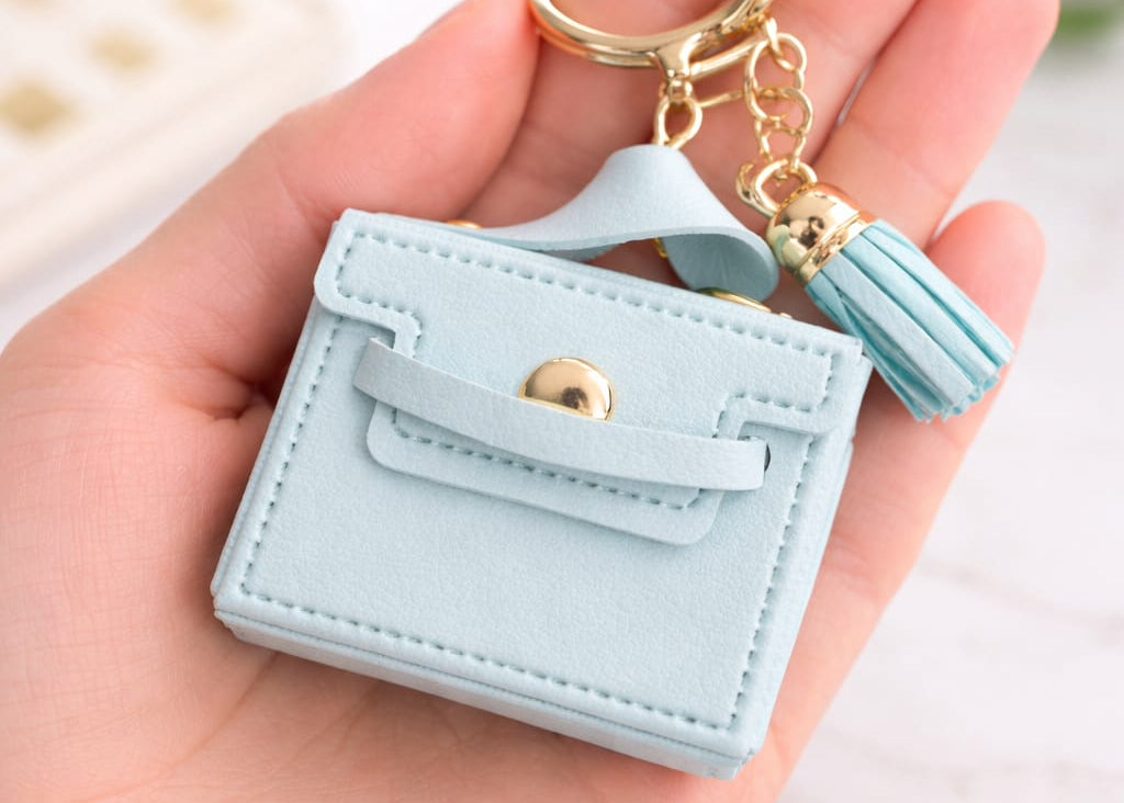 Light blue cardholder with tassel keychain held in a hand on a light background