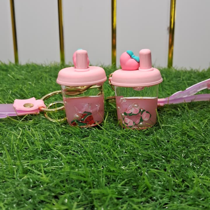 Two pink water bottles with keychains on a grassy surface.